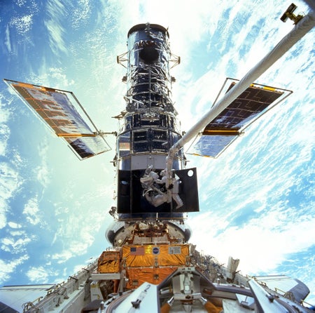 Astronauts repairing the Hubble Space Telescope midflight, with part of the Earth visible below