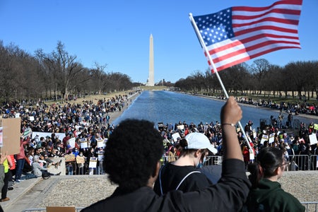 Demonstrators take part in a "Stand Up For Science" rally at the Lincoln Memorial with a man holding a US flag.
