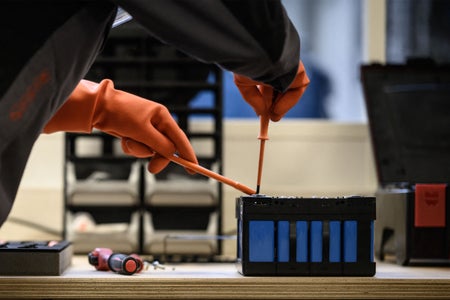 Close up of hands of a mechanic with orange gloves working on a battery module of an electric car.