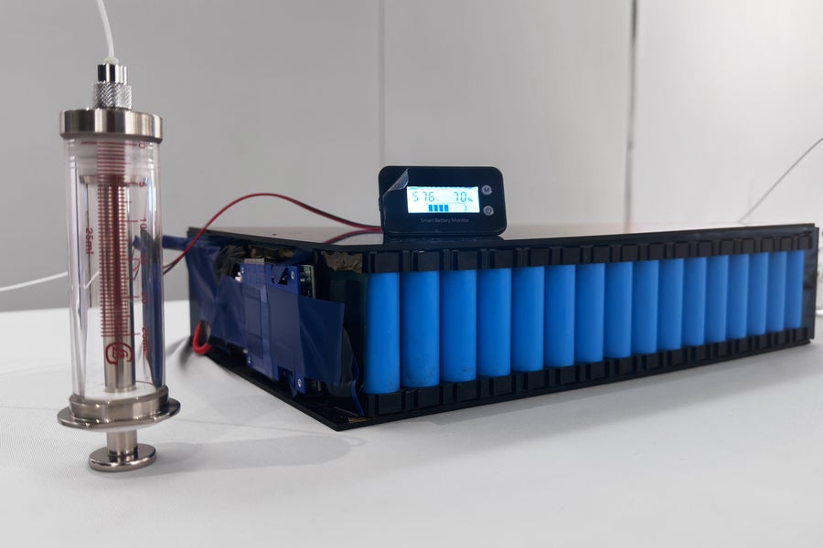 Experimental setup showing electrolyte being injected into a spent blue battery pack on a white lab bench