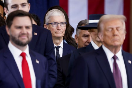 Apple CEO Tim Cook (center, in focus) seen behind US President Donald Trump (right) and US Vice President JD Vance (left), both out of focus, during the presidential inauguration ceremony on January 20, 2025 in Washington DC