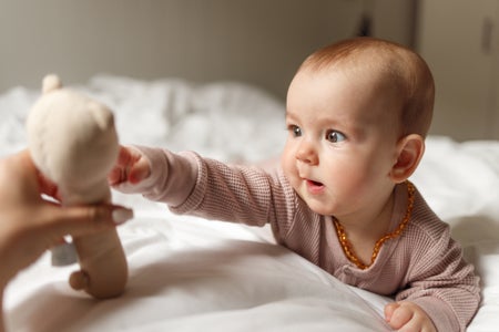 Baby girl playing whit a toy while lying on the bed