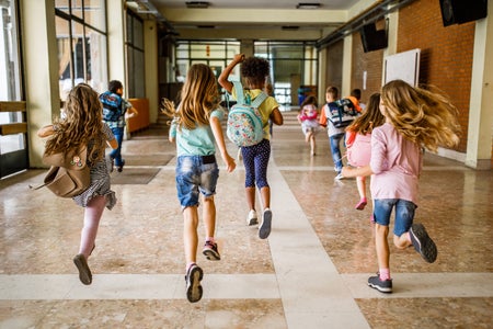 Rear view of group of school children excitedly running down the hallway
