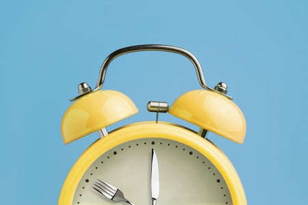 A yellow clock with a fork and knife in place of the hour and minute hands, on a blue background