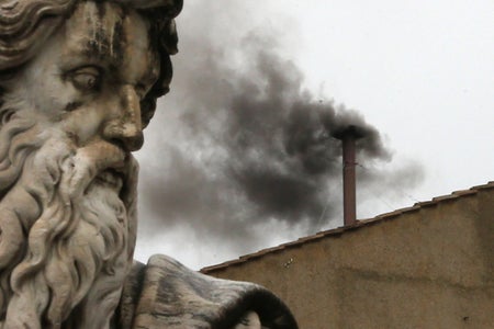 Black smoke billowing from rooftop with statue of bearded man seen in foreground of photo