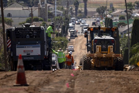 Construction crew working on a road site with visible heat haze distorting the view of the background landscape during a heat wave in Los Angeles