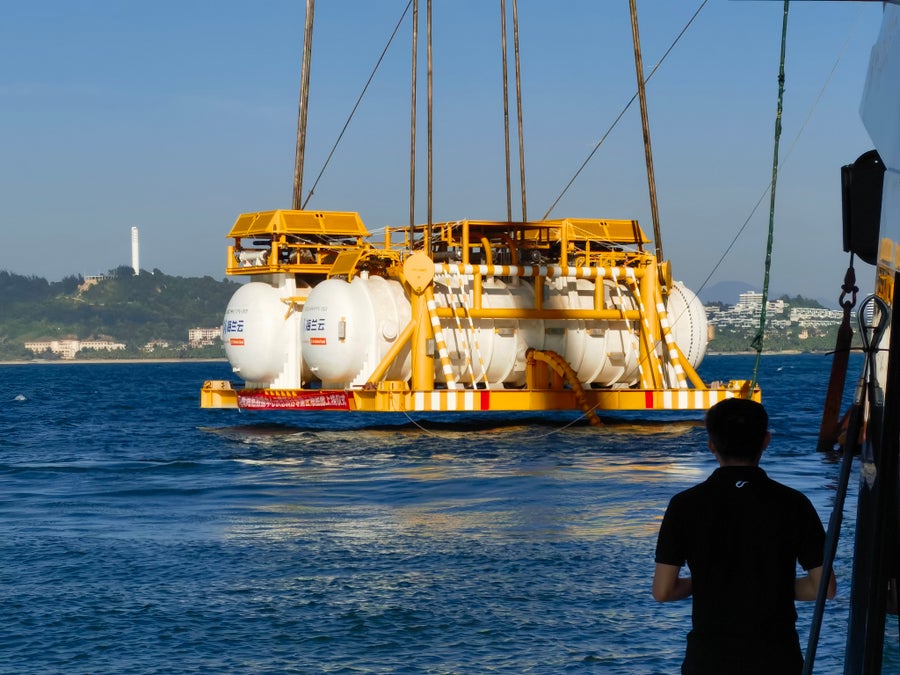 Two white containers suspened by cables above the ocean