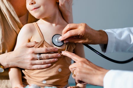 Anonymous doctor holding a stethoscope and listening to lungs of young child sitting on mother's lap