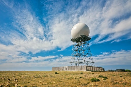 Doppler radar tower in open countryside against a blue clouded sky