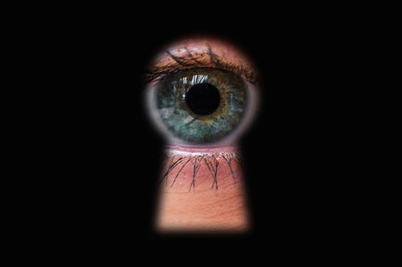 Human eye looking through a keyhole directly toward the camera