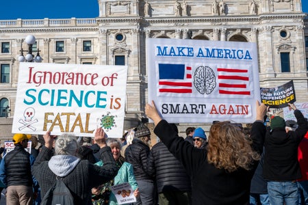 Protesters display signs reading "ignorance of science is fatal" and "make America smart again"