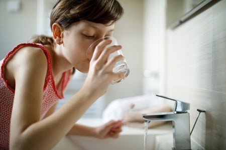 Girl drinking water from glass while holding toothbrush in bathroom