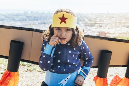 Young girl pointing at camera in homemade superhero costume and cardboard plane wings
