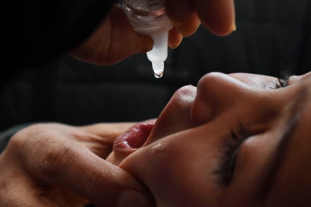 Close up of a healthcare worker using a dropper to administer an oral vaccine to a child