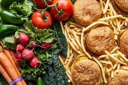 Healthy vs unhealthy food illustrated by vegetables on one side and hamburgers and French fries on the other