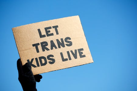Hand holding cardboard sign that reads "LET TRANS KIDS LIVE"