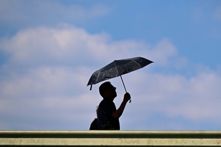 Silhouette of man walking with umbrella against blue sky