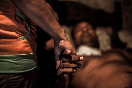 Close up view of a woman's hand holding the hand of a sick man (out of focus) laying in bed