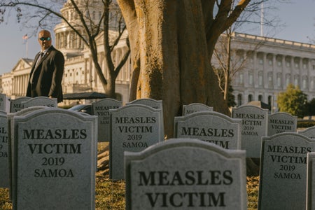 Several fake gravestones reading "Measles victim 2019 Samoa" set up on grass in front of a tree with the US Capitol Building in Washington DC in the background