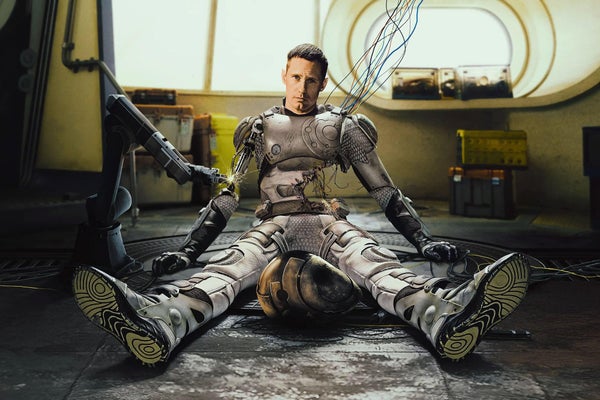 A blend of a robot and man sitting on the floor with legs outstretched and looking at the camera with a plain look.