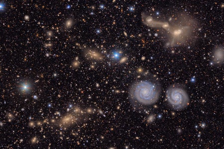 Many stars and galaxies, including two spiral galaxies and three merging galaxies