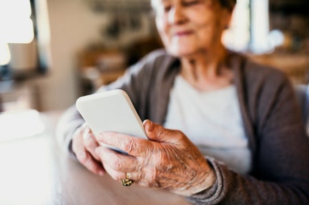 Older woman sitting at a kitchen table while using a smartphone