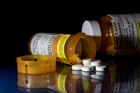 Oxycodone opioid tablets on a reflective surface with prescription bottles laying on their sides against dark background