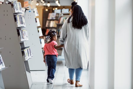 Rear view of a parent and young child holding hands, walking through a public library