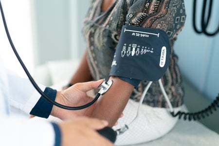 Close up of an older woman sitting on an exam table with a blood pressure cuff on her arm.