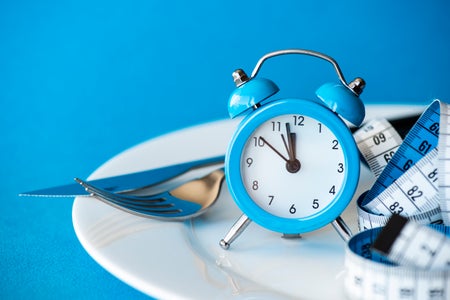 Measuring tape in empty plate with alarm clock, fork and spoon.