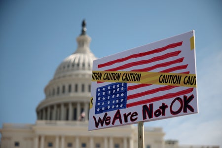 A participant holds a "We are not ok" sign in front of the United States Capitol Building dome