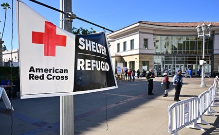 Red cross sign and people are seen outside a wildfire shelter at the Pasadena Convention Center