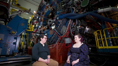 A man and a woman sit in front of a massive machine that has wires and pipes running all over its surface