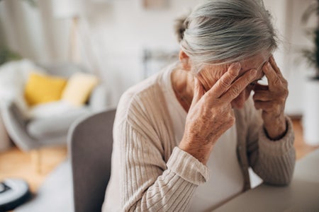 Old woman holding head in pain at home.