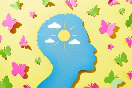 Photo illustration with paper cutout of a man's silhouette in blue on a yellow background with sun and a few clouds in center of head and green and pink butterflies surrounding the head
