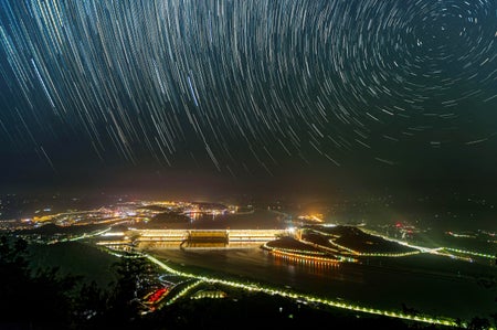 Long exposure photograph at night, revealing rotating star trails in the sky above the Three Gorges Dam in Yichang, Hubei province, China