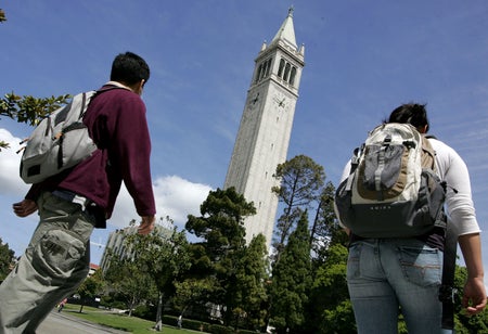 Low angle photograph looking up at Sather Tower on the UC Berkeley campus (center of frame) as students walk by (left and right side of image frame)