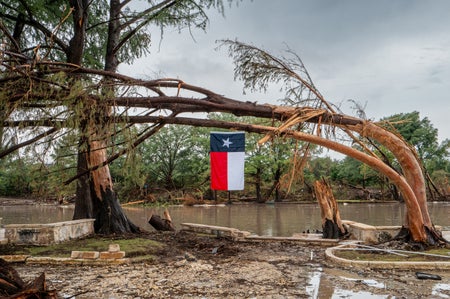 A Texas flag hangs from a storm-damaged tree on the banks of the Guadalupe River on July 13, 2025 in Center Point, Texas