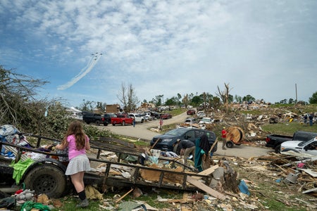 A U.S. Air Force aerobatic team flies in formation over community members and crews cleaning up debris in the community of Sunshine Hills outside of London, Kentucky after a tornado caused wide scale destruction