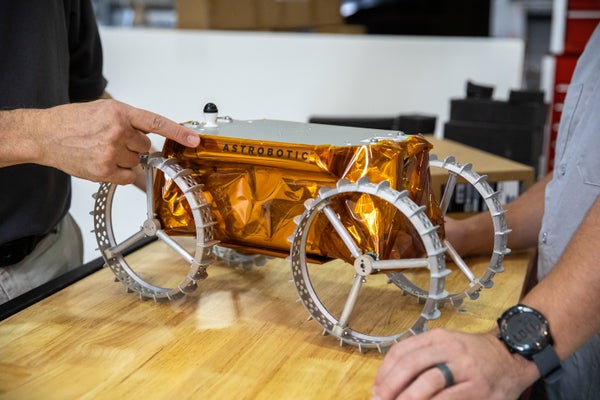 Metallic rover roughly the size of a shoebox sitting on a table