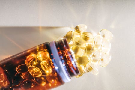 Golden vitamin d pills spilling from brown bottle onto brightly lit surface
