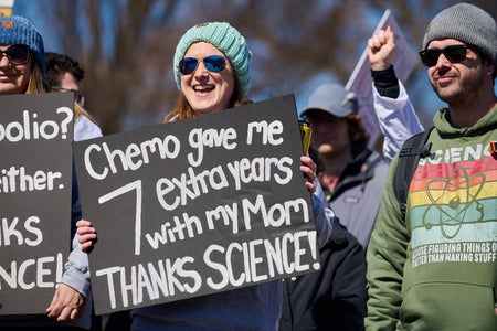 Woman at rally holds sign reading "Chemo gave me 7 extra years with my Mom. THANKS SCIENCE!"
