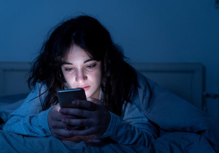 Young woman in bed scrolling on iphone.