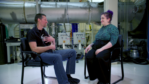 An image of two people sitting on chairs inside MIT LIGO Lab.
